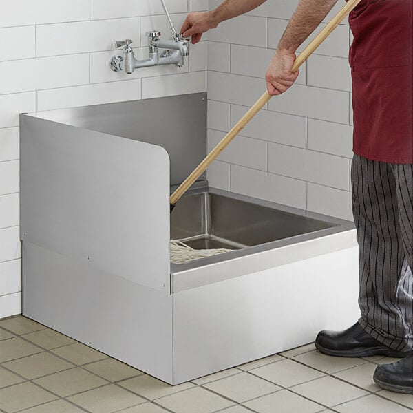 A man cleaning a Regency stainless steel mop sink with a mop.