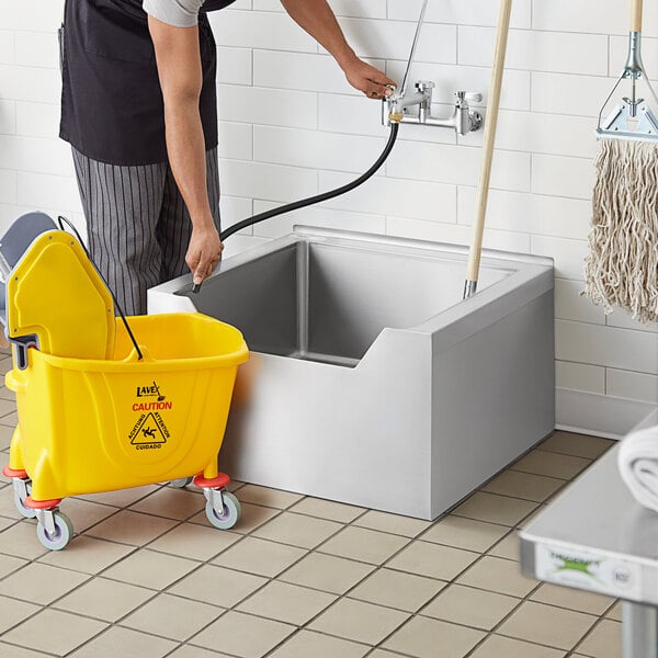 A man using a Regency mop sink to clean a bathroom.
