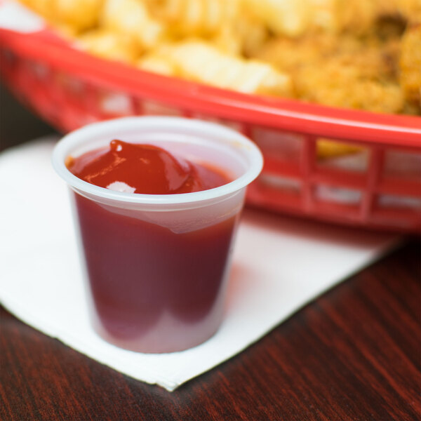 A Solo translucent plastic souffle cup of ketchup next to a basket of fries.