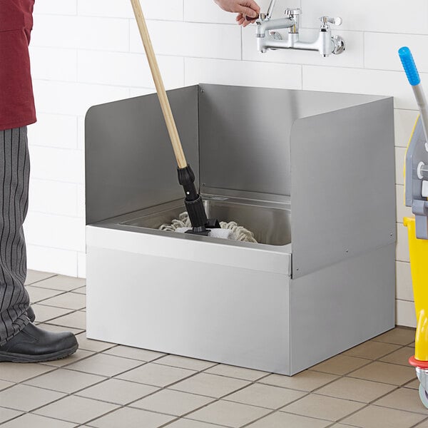 A person using a Regency stainless steel three-sided splash for a mop sink to clean a mop in a sink.