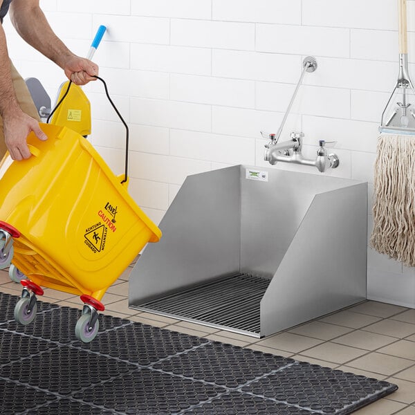 A man using a Regency floor mounted mop sink to fill a yellow bucket.
