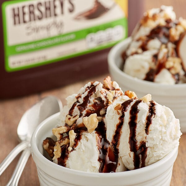 A bowl of ice cream with HERSHEY'S chocolate syrup and walnuts.