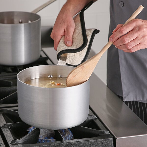 A person cooking soup in a Choice aluminum sauce pan on a stove.