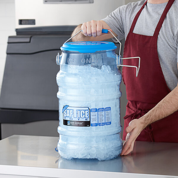 A man holding a San Jamar Saf-T-Ice 6 gallon blue plastic ice tote filled with ice.
