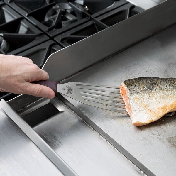 A person using a Mercer Culinary Hell's Handle fish turner to grill fish.