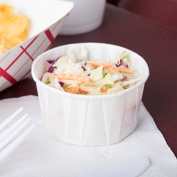 A Solo white paper souffle cup filled with coleslaw on a table in a food truck.