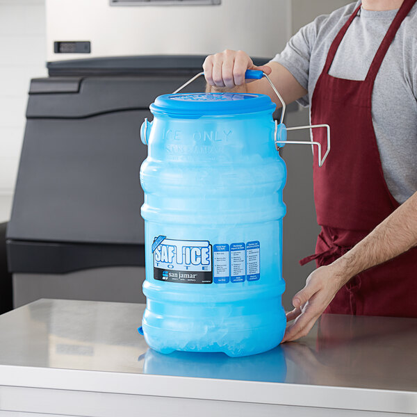 A person in an apron holding a blue San Jamar ice bucket with a lid.