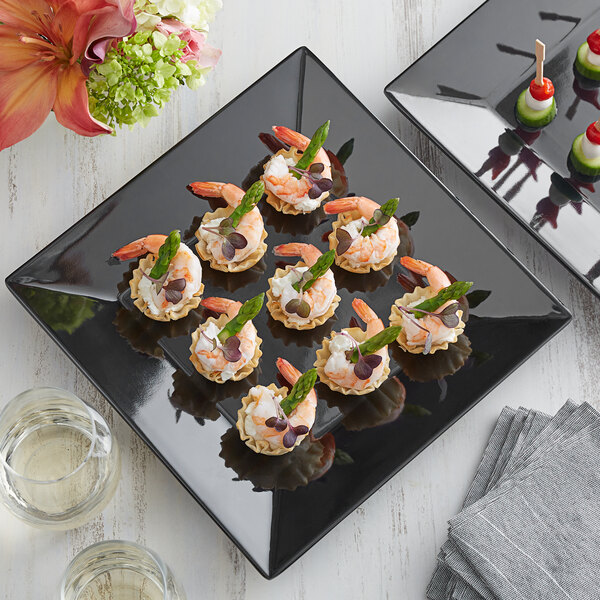 An Acopa Rittenhouse black square melamine plate with shrimp and asparagus and other appetizers on a table.
