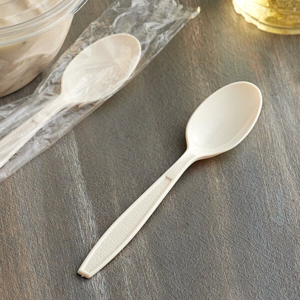 A Visions beige heavy weight plastic spoon in a plastic bag next to a bowl of soup.