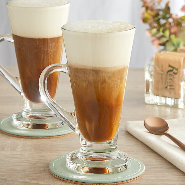 Two Acopa Select glass Irish coffee mugs with a drink inside.