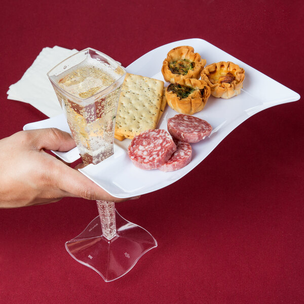 A hand holding a white plastic cocktail plate with a glass of champagne on it.