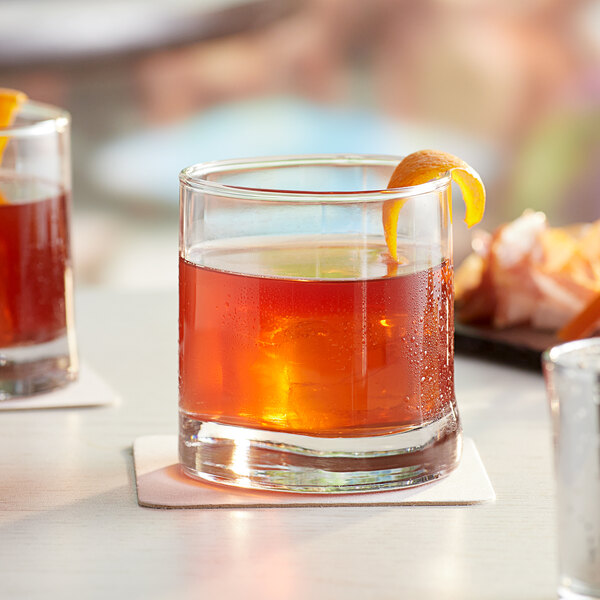 A group of Acopa Bermuda rocks glasses filled with amber drinks and garnished with orange peels.