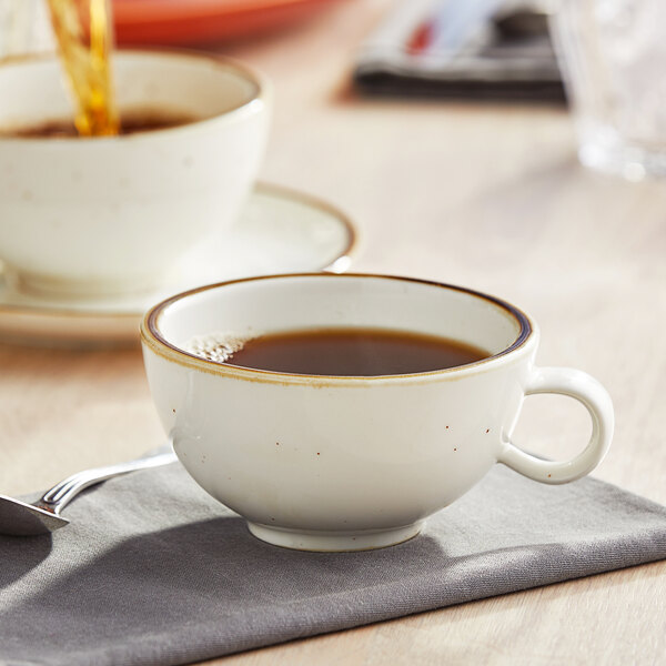 A cup of coffee on a table with a Vanilla Bean Stoneware Low Cup and a spoon.