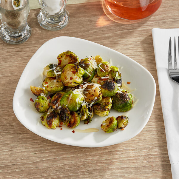 A plate of brussels sprouts on an Acopa cream white stoneware plate on a table.