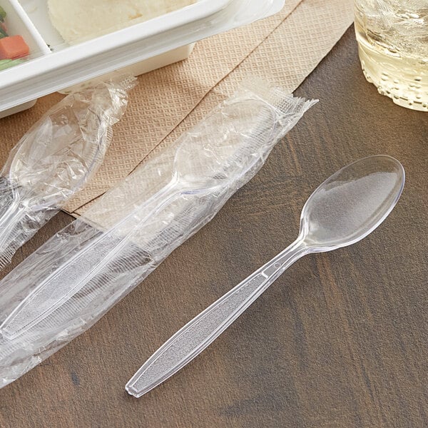 A plastic container of individually wrapped Visions clear heavy weight plastic spoons on a table.