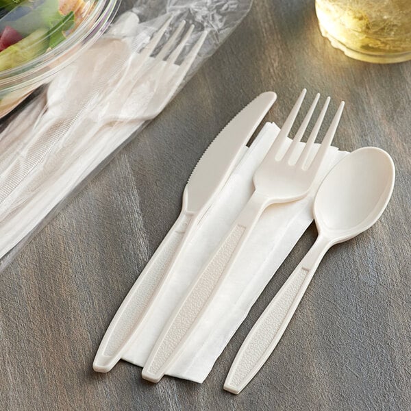 A wrapped plastic Visions fork and knife on a napkin next to a bowl of salad.
