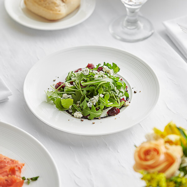 An Acopa Liana bright white porcelain plate with embossed lines full of salad on a table.