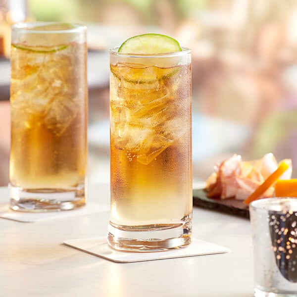 A pair of Acopa Bermuda beverage glasses filled with iced tea and lime slices on a table.