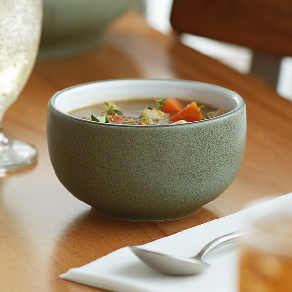 An Acopa Embers moss green stoneware bowl filled with vegetable soup on a table.