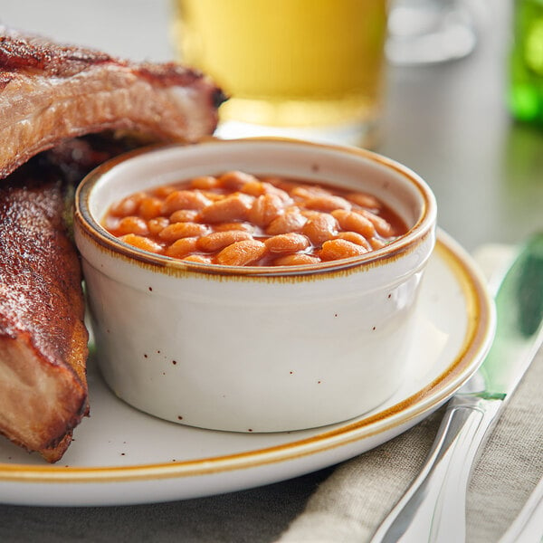 A plate of ribs and beans with a bowl of beans in a yellow stoneware bowl.