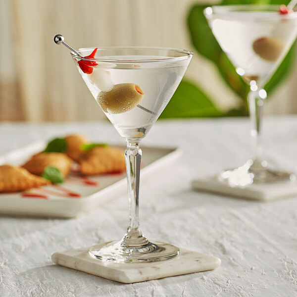 A close-up of two Acopa Empire martini glasses with olives and a garnish on a table.