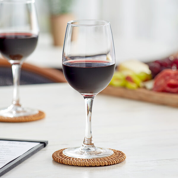 Two Acopa Select Flora wine glasses on a wooden coaster on a table with a glass of red wine.