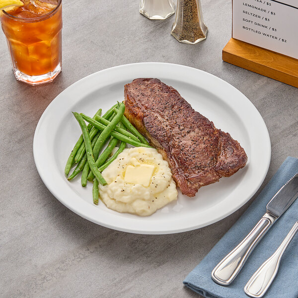 An Acopa narrow rim stoneware plate with steak, mashed potatoes, and green beans.