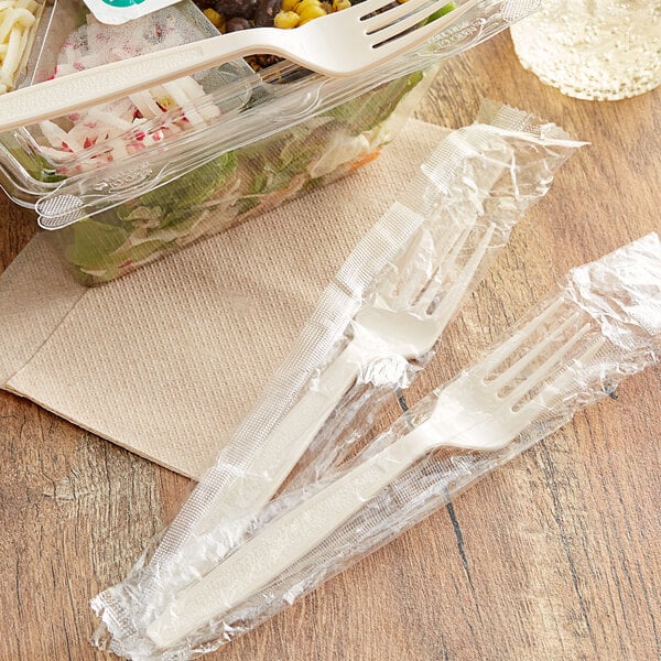Individually wrapped Visions beige plastic forks next to a salad in a plastic container.