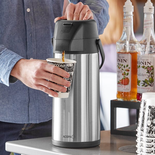 A person pouring coffee from a stainless steel Acopa airpot into a cup.