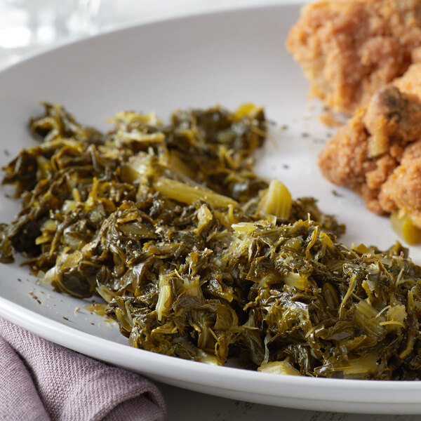 A plate of fried chicken and chopped mustard greens on a table.
