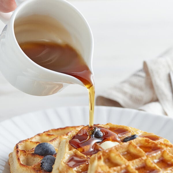 A person pouring Butternut Mountain Farm Grade A Amber Pure Vermont Maple Syrup on a waffle.