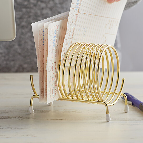 A hand holding a stack of paper in a Choice brass-plated check caddy.