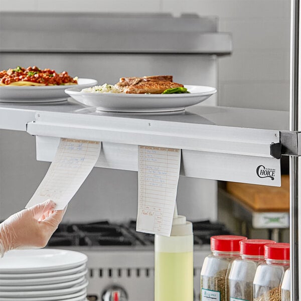 A person using a Choice aluminum wall mounted ticket holder to hold a paper over a plate of food.