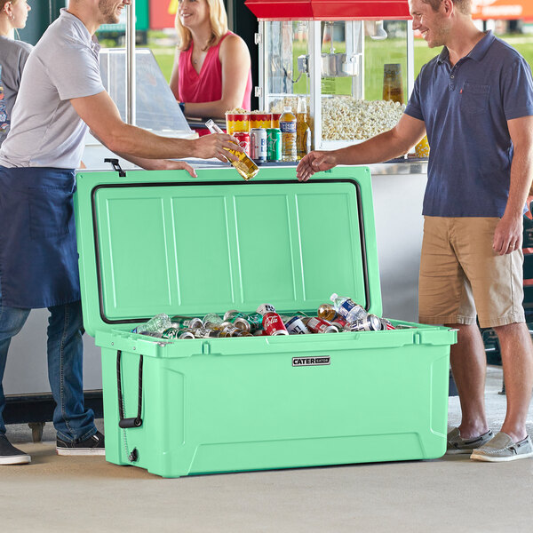 A group of men standing next to a CaterGator seafoam green cooler filled with cans and bottles.