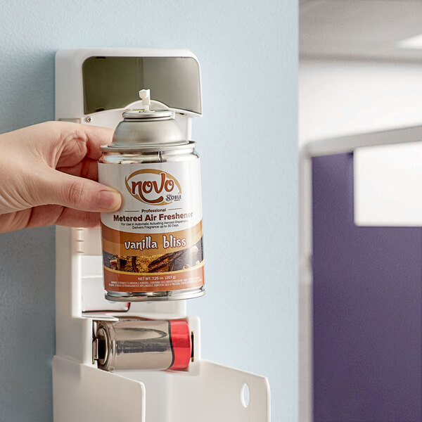 A hand holding a Noble Chemical Novo Vanilla Bliss air freshener refill can.