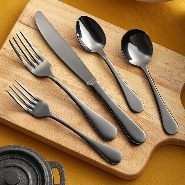 Acopa Vernon Black stainless steel spoon, fork, and knife on a wooden cutting board.