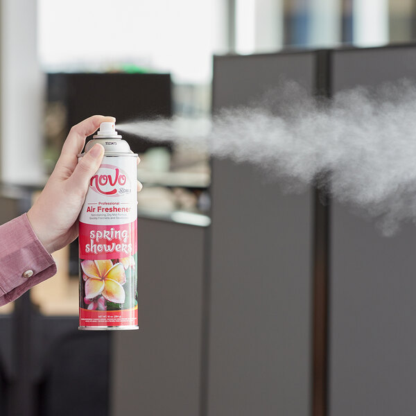 A person using a red and white can of Noble Chemical Novo Spring Showers air freshener.