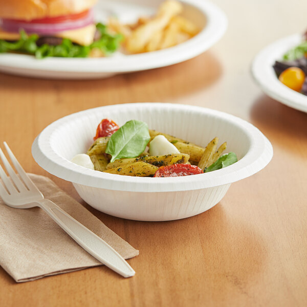 A Pactiv EarthChoice white compostable paper bowl filled with pasta, basil, and tomatoes on a table with a fork.