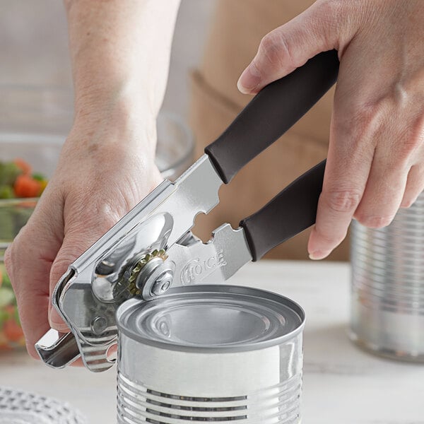 A person using a Choice manual can opener with a black handle to open a can.