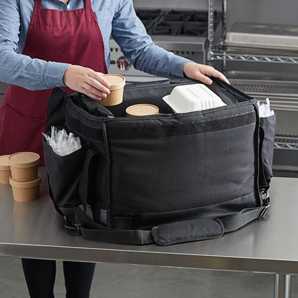 A person in a red apron putting food in a Vesture black bag.
