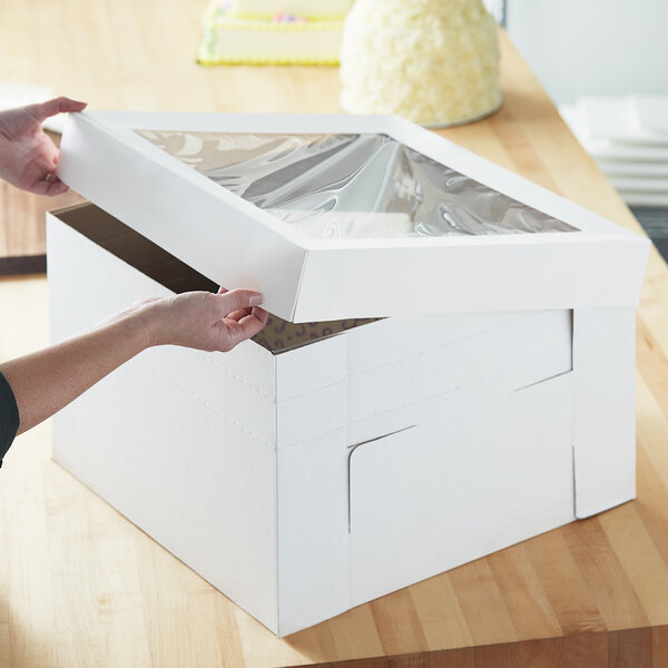 A person opening a white Enjay Flexbox bakery box with a cake inside.