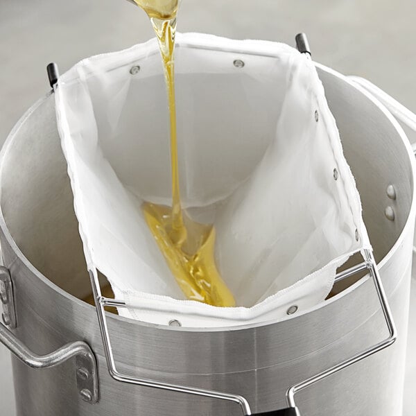 A person using a 7 1/2" deep fryer oil filter bag to pour yellow liquid into a metal container.