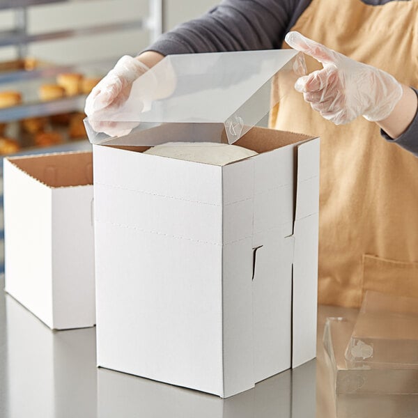 A person in an apron and gloves opening a white Enjay Flexbox bakery box.