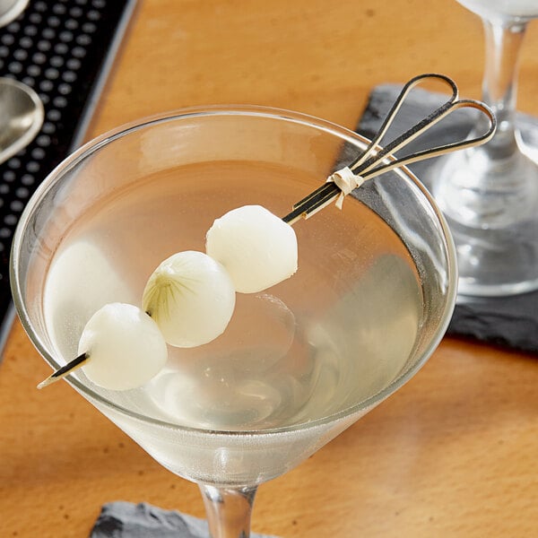 A glass with a drink and a black bamboo heart skewer with three white onions on it.