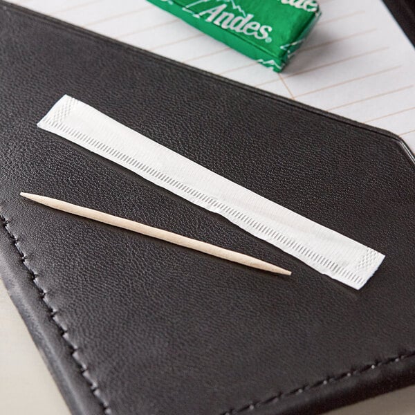 A toothpick in a white paper wrapper on a black leather cover.