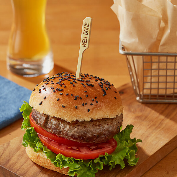 A burger on a wooden board with a Bamboo by EcoChoice Well Meat Marker in it.