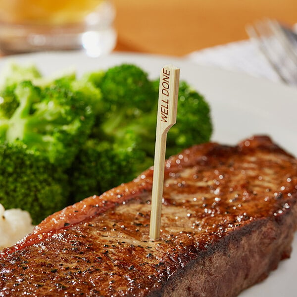 A steak with a Bamboo by EcoChoice "Well" Meat Marker in it on a plate of broccoli.