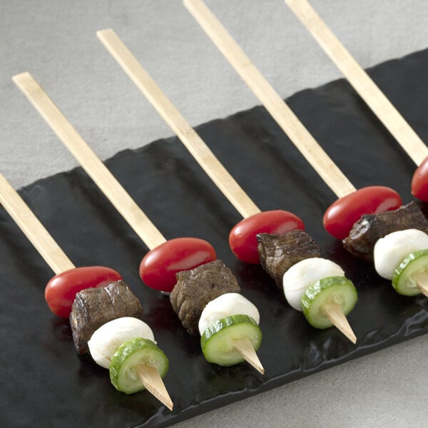 A black plate with Bamboo by EcoChoice Natural Bamboo Skewers holding meat, tomatoes, cucumbers, and cheese.