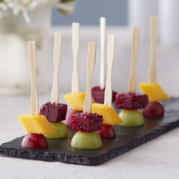 Choice Compostable bamboo fruit picks in a tray of fruit on a black plate.