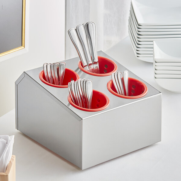 A stainless steel flatware organizer with red perforated plastic cylinders holding silverware.